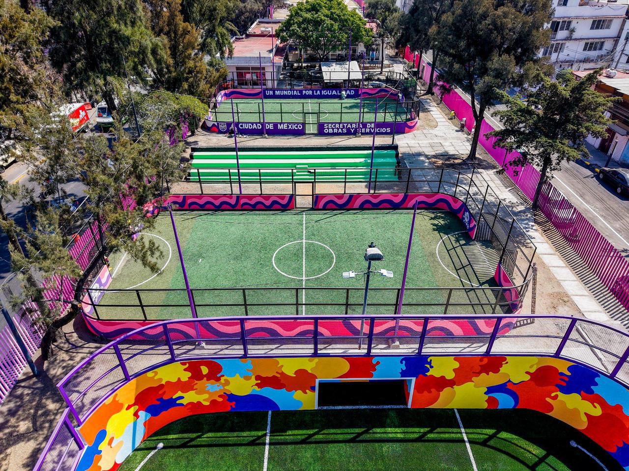 : Vista Aérea De Canchas De Fútbol Rápido Rehabilitadas En Iztapalapa, Ciudad De México. Las Canchas Presentan Pasto Sintético Profesional Y Muros Perimetrales Decorados Con Murales Coloridos En Tonos Morados, Rosas Y Amarillos. Se Observa Un Letrero Que Dice &Quot;Un Mundial Por La Igualdad&Quot; Y Logos De La Secretaría De Obras Y Servicios. La Infraestructura Está Rodeada De Árboles Y Áreas Urbanas Mejoradas.
