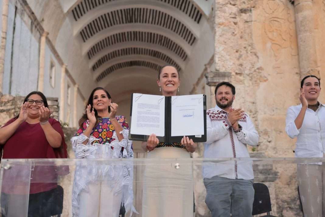 La Presidenta De México, Claudia Sheinbaum Pardo, Posa En El Centro De Un Presídium Elevado, Sosteniendo Y Mostrando Una Carpeta Abierta Con El Decreto De Creación De Destinos Turísticos Comunitarios Firmado.