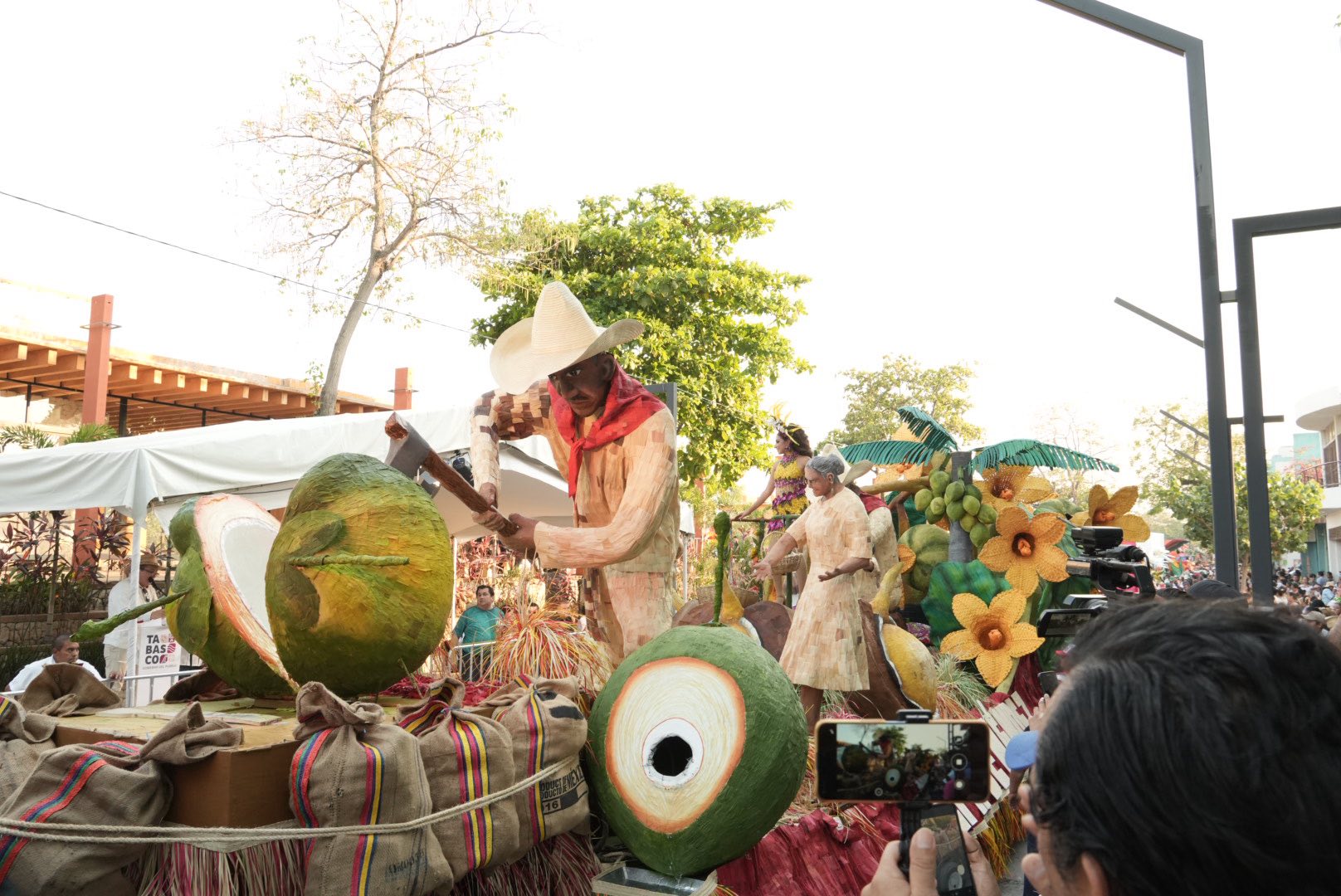 Una Toma De Ángulo Medio A Bajo Del Monumental Carro Alegórico &Quot;El Coprero&Quot; Del Municipio De Jalpa De Méndez Durante Un Desfile. En El Centro, Un Hombre Con Ropa Tradicional Beige Y Faja Blanca Sonríe Mientras Sostiene En Alto El Trofeo De Madera Del Primer Lugar.