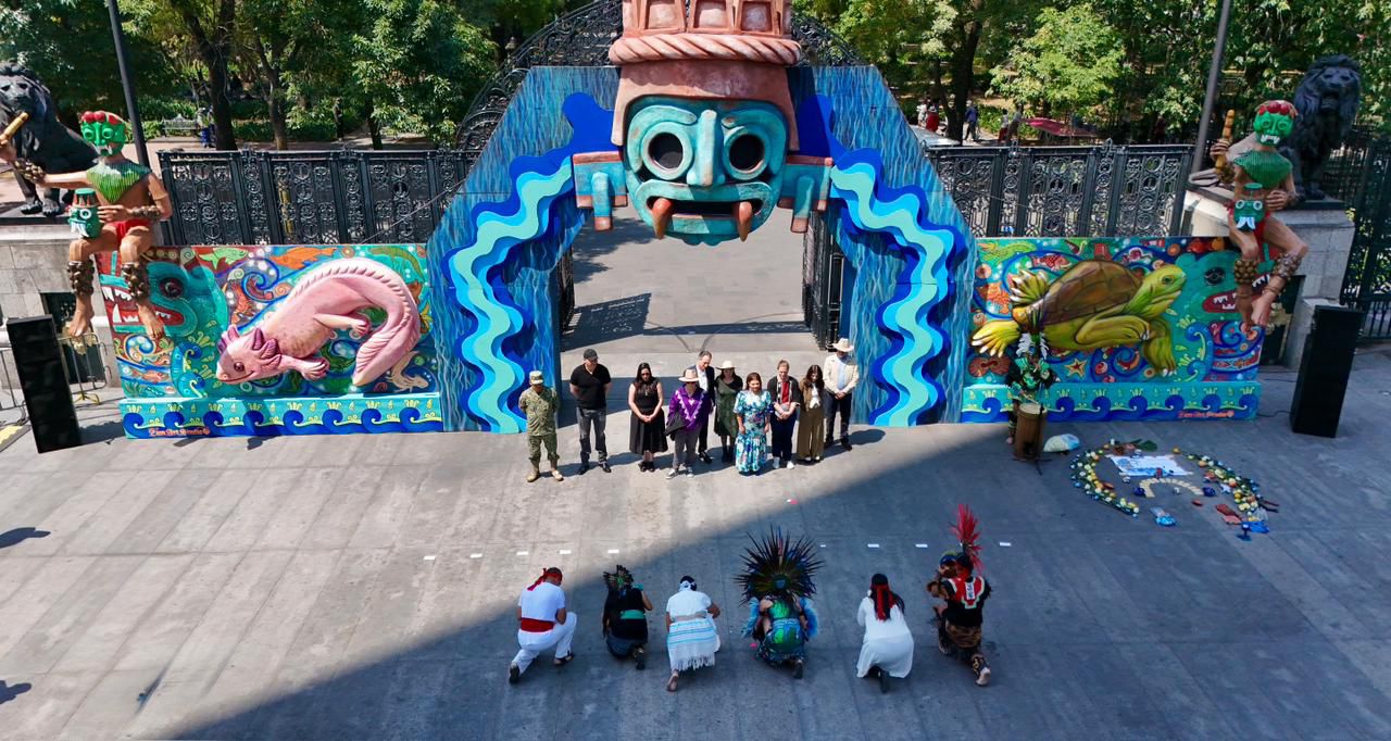 Clara brugada inaugura aqüifera 2026: inversión histórica para el agua en cdmx la revista del sureste mx Una Toma Aérea De Ángulo Alto De La Entrada Al Festival Del Bosque 2026. La Entrada Es Un Gran Arco Azul Adornado Con Patrones De Ondas Azules Y Una Gran Máscara Prehispánica En La Parte Superior. A Cada Lado Del Arco Hay Murales Vibrantes, Uno Que Representa Un Ajolote Rosa Y El Otro Una Tortuga Verde.