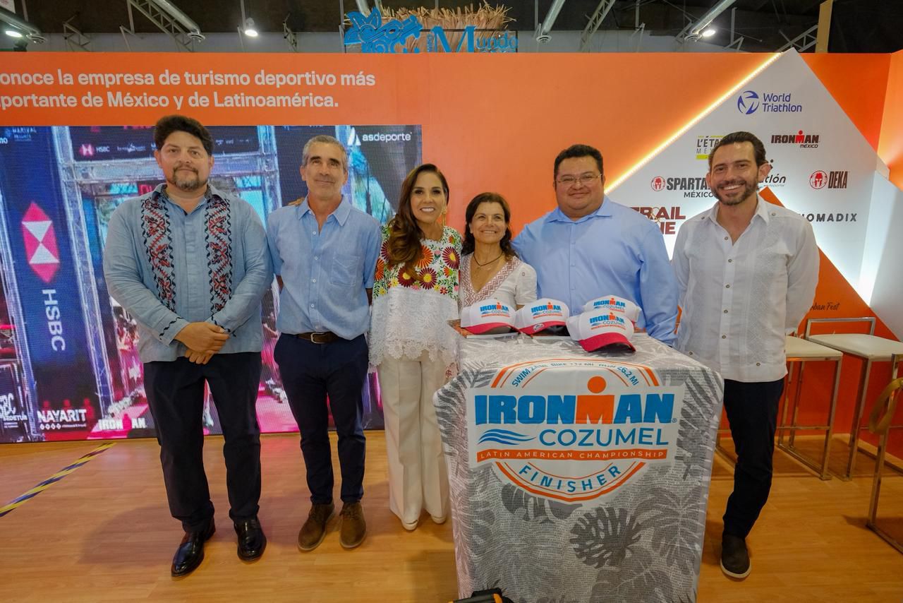 La Gobernadora Mara Lezama Espinosa, Junto A La Comitiva De Quintana Roo Y Modelos Con Trajes Regionales Y De Fantasía Inspirados En El Mar, Posan En El Pabellón Del Caribe Mexicano. Al Centro Destaca Una Mesa Con Folletos Turísticos De Destinos Como Isla Mujeres Y Bacalar.