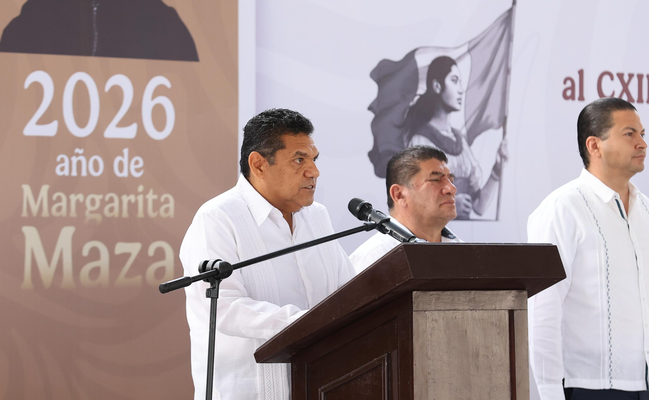 El Gobernador De Tabasco, Javier May Rodríguez, Brindando Un Discurso Desde Un Podio De Madera Durante Un Evento Oficial. Al Fondo Se Observa Un Gráfico Institucional Con La Leyenda &Quot;2026 Año De Margarita Maza&Quot; Y Una Ilustración Conmemorativa.