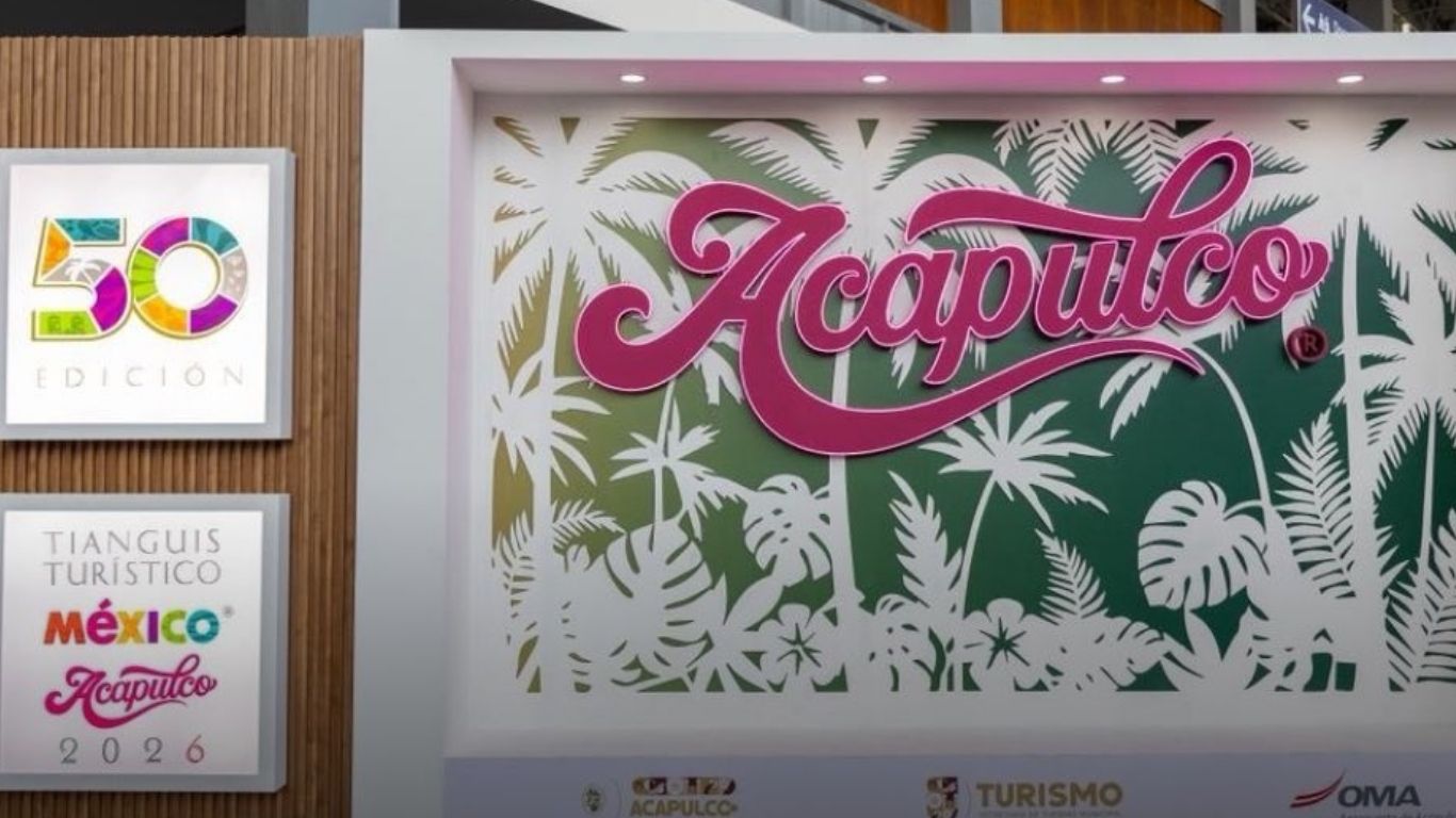 Fotografía Del Stand Promocional De Acapulco Para La Edición 50 Del Tianguis Turístico México 2026. Se Observa Un Muro Blanco Decorado Con Siluetas De Palmeras Y Hojas Tropicales En Verde Y Dorado. En El Centro, Destaca El Nombre &Amp;Quot;Acapulco&Amp;Quot; En Una Tipografía Cursiva Color Rosa Vibrante.