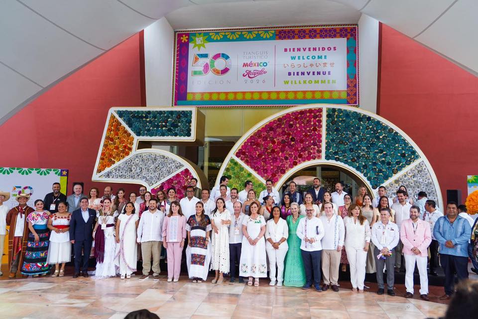 Una Toma Amplia Y Colorida De La Ceremonia De Inauguración De La Edición 50 Del Tianguis Turístico México 2026 En Acapulco. Docenas De Dignatarios, Funcionarios Y Asistentes Están De Pie En Filas Sobre Un Piso De Mármol, Posando Frente A Una Enorme Estructura Escultórica Del Número &Quot;50&Quot;. La Estructura Está Dividida En Dos Secciones Grandes Y Arqueadas; La De La Izquierda Está Cubierta De Flores Naranjas Y Amarillas, Y La De La Derecha Está Cubierta De Flores Azul Verdosas.