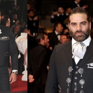 Alejandro nones impacta en el festival de cannes 2026 vestido con traje de charro la revista del sureste mx Otografía De Plano Entero Del Actor Alejandro Nones Posando De Pie En El Centro De La Alfombra Roja Del Festival De Cannes. Viste Un Elegante Traje De Charro Mexicano De Gran Gala En Color Negro Con Sutiles Rayas Diplomáticas, Botonadura De Plata En El Chaleco Y Detalles Bordados Tradicionales A Los Costados Del Pantalón. Lleva Una Camisa Blanca Con Un Moño O Corbatón De Charro Claro Y Mantiene Las Manos Cruzadas Al Frente. Al Fondo Se Observa A Otros Asistentes Y Fotógrafos Desenfocados.