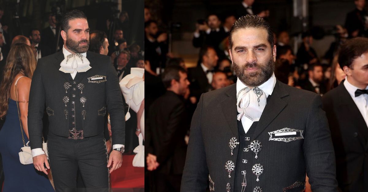 Alejandro nones impacta en el festival de cannes 2026 vestido con traje de charro la revista del sureste mx Otografía De Plano Entero Del Actor Alejandro Nones Posando De Pie En El Centro De La Alfombra Roja Del Festival De Cannes. Viste Un Elegante Traje De Charro Mexicano De Gran Gala En Color Negro Con Sutiles Rayas Diplomáticas, Botonadura De Plata En El Chaleco Y Detalles Bordados Tradicionales A Los Costados Del Pantalón. Lleva Una Camisa Blanca Con Un Moño O Corbatón De Charro Claro Y Mantiene Las Manos Cruzadas Al Frente. Al Fondo Se Observa A Otros Asistentes Y Fotógrafos Desenfocados.