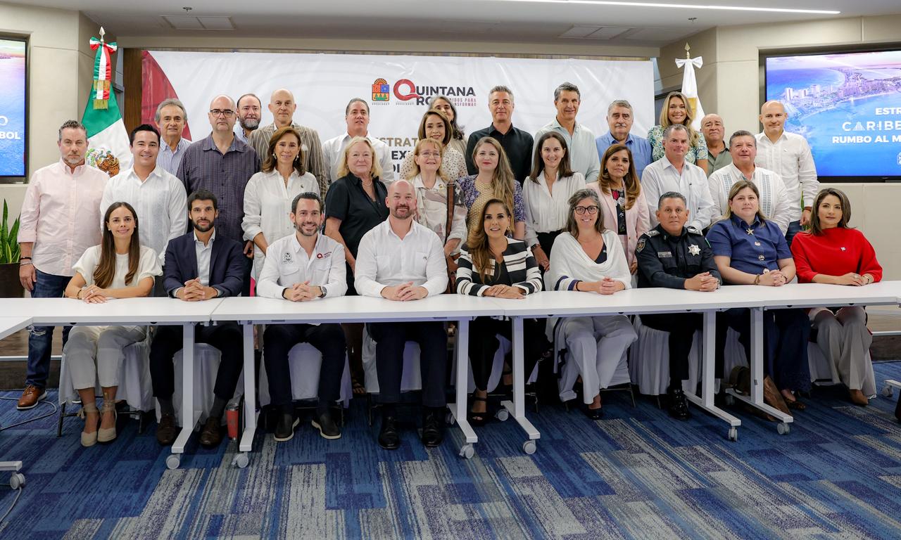 Una Amplia Toma Fotográfica De Plano General En Una Sala De Juntas Moderna Y Tecnológica. Alrededor De Una Gran Mesa Blanca En Forma De &Quot;U&Quot;, Se Encuentran Más De 30 Personas, Incluyendo Autoridades Estatales, Municipales Y Representantes Del Cuerpo Consular. En El Centro De La Mesa Principal Están Sentadas La Gobernadora Mara Lezama Y La Presidenta Municipal Ana Paty Peralta, Junto A Otros Funcionarios De Alto Rango. Al Fondo, Un Telón Blanco Muestra El Logotipo De Quintana Roo.