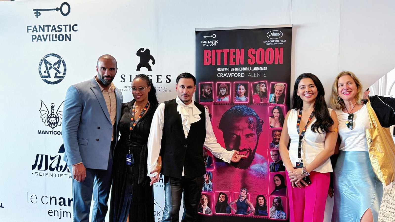 De méxico a cannes: lauand omar sacude el fantastic pavilion 2026 con "bitten soon", una sátira de vampiros y horror político la revista del sureste mx Fotografía En Plano Entero Que Muestra A Seis Personas Posando Alineadas En Un Evento Promocional Frente A Un Fondo Blanco Con Logotipos Comerciales, Entre Los Que Destaca &Quot;Fantastic Pavilion&Quot;. En El Centro De La Imagen Hay Un Póster Vertical De Color Negro Y Rosa Con El Título &Quot;Bitten Soon&Quot;, El Cual Muestra El Rostro De Un Hombre Con Colmillos De Vampiro Rodeado De Pequeños Retratos De Elenco.