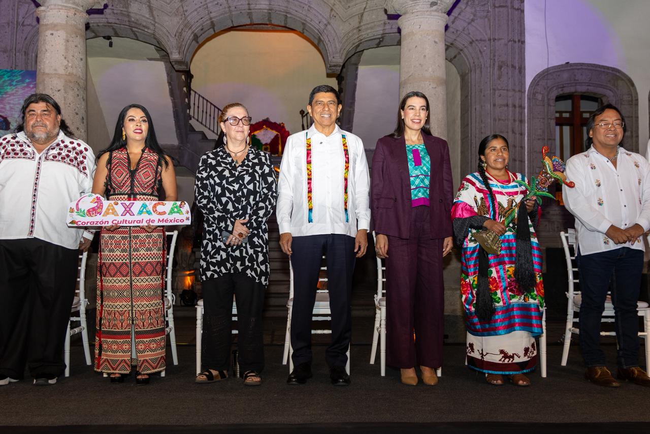 Fotografía Grupal De Autoridades Y Representantes Durante La Presentación De La Guelaguetza 2026 En Un Escenario Interior. Al Centro, El Gobernador Salomón Jara Cruz Viste Una Guayabera Blanca Con Bordados Tradicionales, Flanqueado Por Funcionarios Y Representantes Indígenas Que Visten Trajes Típicos Coloridos De Las Regiones De Oaxaca.