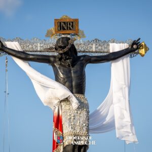 Una Toma De Plano Medio Del Cristo Negro De San Román, Una Escultura Religiosa De Ébano O Madera Oscura, Crucificada En Una Cruz Adornada Con Intrincados Detalles De Plata. La Figura De Cristo Viste Un Perizoma (Paño De Pureza) Blanco Bordado Con Pedrería Y Perlas, Y Tiene Una Tela Blanca Larga Y Ligera Que Cuelga Elegantemente De Sus Brazos Extendidos.