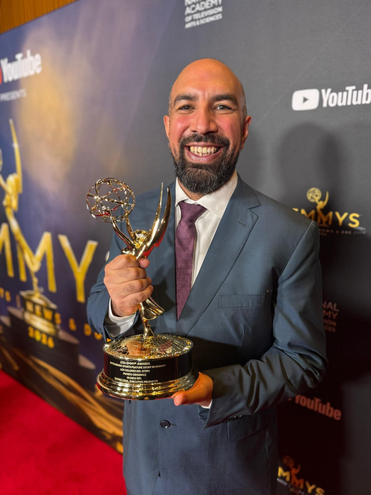 Orgullo nacional: el documental mexicano ‘los colores del istmo’ de nfl méxico es galardonado en los sports emmy awards la revista del sureste mx Izamná Crail Con El Premio Sports Emmy Por ‘Los Colores Del Istmo’
(Archivo: El Documental Mexicano ‘Los Colores Del Istmo’ De Nfl México Es Galardonado En Los Sports Emmy Awards.jpg)
Texto Alternativo: Fotografía En Plano Medio Y Formato Vertical Tomada En Interiores Durante Una Alfombra Roja. En El Centro De La Imagen, El Director De Marketing De Nfl México Y Productor Ejecutivo, Izamná Crail, Sonríe Ampliamente A La Cámara Mostrando Orgullo. Es Un Hombre De Tez Morena Clara, Calvo Y Con Barba Oscura Bien Recortada, Que Viste Un Traje Sastre Color Gris Azulado, Camisa Blanca Y Corbata Color Vino. Con Ambas Manos Sostiene Firmemente La Estatuilla Dorada De Un Premio Sports Emmy, Cuya Placa Grabada Revela Los Detalles De La Categoría Ganadora. El Fondo Muestra Un Panel Publicitario Oscuro De Los &Quot;Emmys Sports, News &Amp; Documentary 2026&Quot; Con Logotipos Repetidos De Youtube.