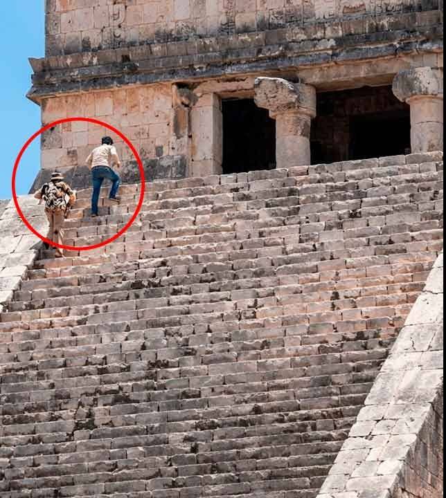 Fotografía En Plano Contrapicado Que Captura La Escalinata De Piedra De La Pirámide Arqueológica De Kukulkán (&Quot;El Castillo&Quot;) En Chichén Itzá, Yucatán, Bajo Un Cielo Azul Despejado. En La Zona Superior Izquierda Del Monumento, Cerca De La Entrada Del Templo Superior, Se Observa A Dos Turistas De Espaldas Ascendiendo De Manera Ilegal Por Los Desgastados Escalones; Uno Viste Playera Clara Con Jeans De Mezclilla Y El Otro Porta Un Sombrero De Ala Ancha Con Una Mochila Estampada. Ambas Personas Se Encuentran Encerradas Dentro De Un Círculo Rojo Grueso Que Resalta La Infracción Cometida En El Área Restringida.