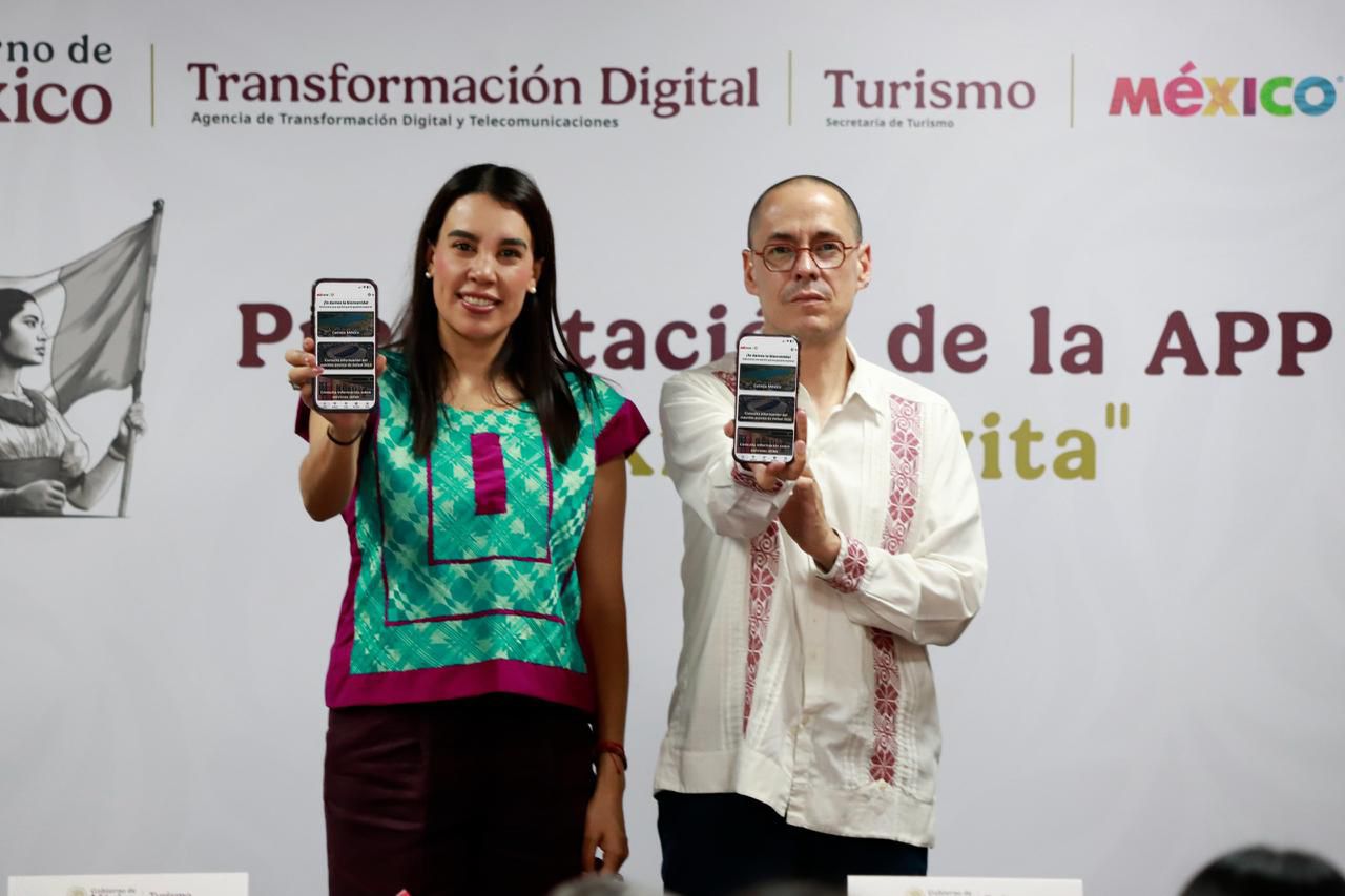 Fotografía De Plano Medio Y Toma Frontal En Interiores. La Secretaria De Turismo, Josefina Rodríguez Zamora, Y El Titular De La Agencia De Transformación Digital, José Antonio Peña Merino, Posan De Pie Sosteniendo Cada Uno Un Teléfono Celular Orientado Hacia La Cámara, Mostrando En Las Pantallas La Interfaz De Usuario De La Nueva Aplicación Móvil. Rodríguez Zamora, A La Izquierda, Viste Una Blusa Tradicional Mexicana Bordada En Tonos Verde Y Rosa Con Pantalón Oscuro. Peña Merino, A La Derecha, Usa Una Guayabera Blanca Con Detalles Bordados En Color Vino. Al Fondo, Un Muro Blanco Exhibe Los Logotipos Institucionales De La Agencia De Transformación Digital Y Telecomunicaciones, La Secretaría De Turismo Y La Marca &Quot;México&Quot;, Junto Con Un Fragmento Del Texto &Quot;Presentación De La App México Invita&Quot;.