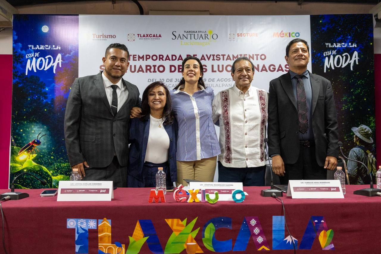 Fotografía En Plano Medio Y De Frente De Cinco Funcionarios Públicos De Pie Detrás De Una Mesa De Presídium Con Mantel Guinda Que Muestra Las Letras Coloridas De &Quot;Tlaxcala&Quot;. De Izquierda A Derecha Aparecen Un Hombre Con Traje Oscuro; La Gobernadora Lorena Cuéllar Cisneros Con Saco Azul; La Secretaria De Turismo Federal, Josefina Rodríguez Zamora.