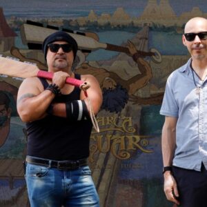 Orgullo nacional en cannes: "la marca del jaguar" de víctor mayorga conquista el marché du film con una épica mexica de animación la revista del sureste mx Fotografía De Prensa En Plano Medio Que Muestra A Dos Hombres Posando De Pie Bajo La Luz Del Sol Frente A Un Gran Muro Promocional Ilustrado.