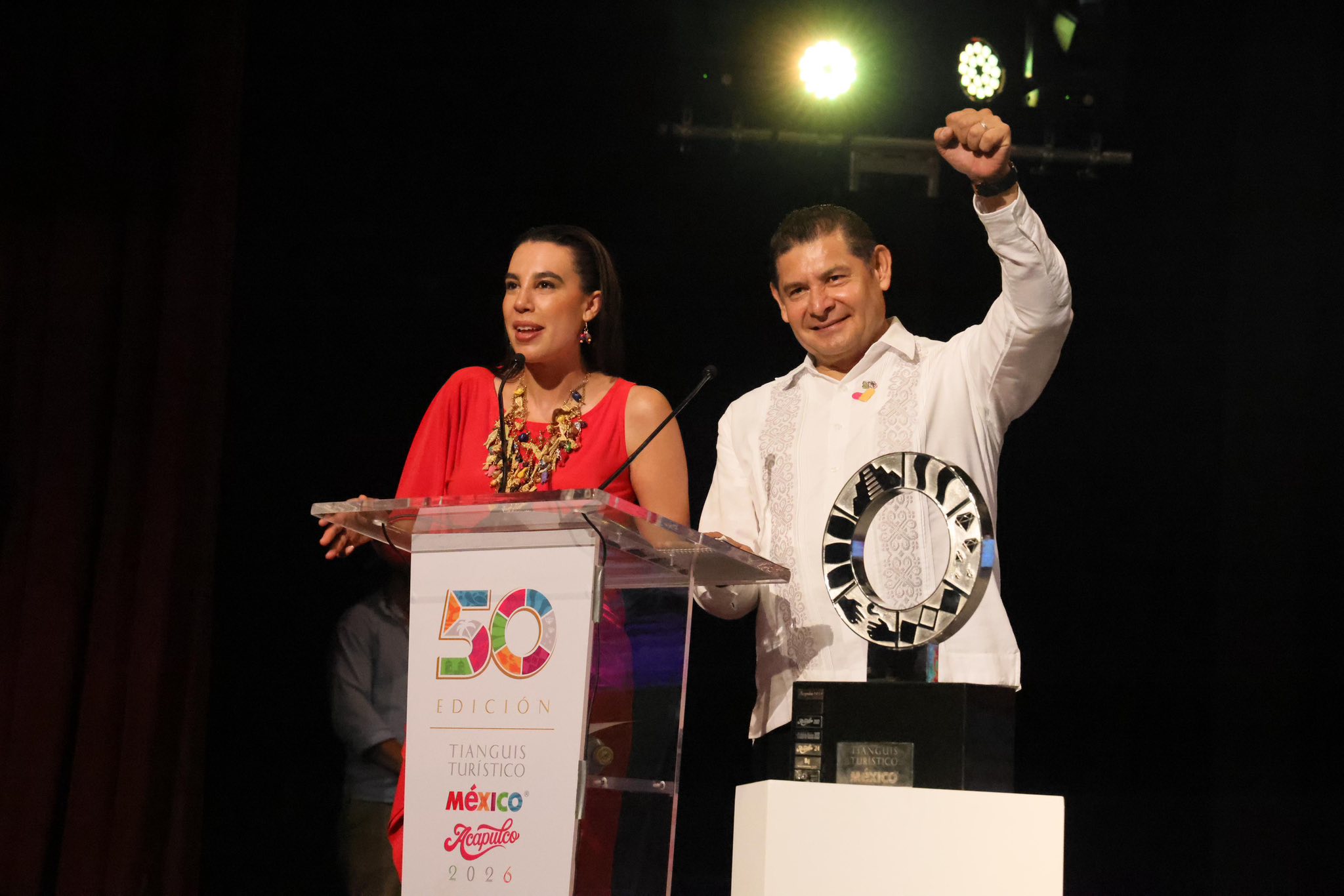 Aquí Tienes El Texto Alternativo Y La Leyenda Para La Imagen, Basados En El Acto Oficial De Relevo De Sede:

Texto Alternativo (Alt Text)
Josefina Rodríguez Zamora, Secretaria De Turismo, Y Alejandro Armenta, Gobernador De Puebla, En Un Estrado Durante El Tianguis Turístico 2026 En Acapulco. Rodríguez Zamora Habla Tras Un Podio Con El Logotipo De La 50 Edición Del Evento, Mientras Armenta Levanta El Puño En Señal De Triunfo Junto Al Trofeo De La Estafeta Turística.