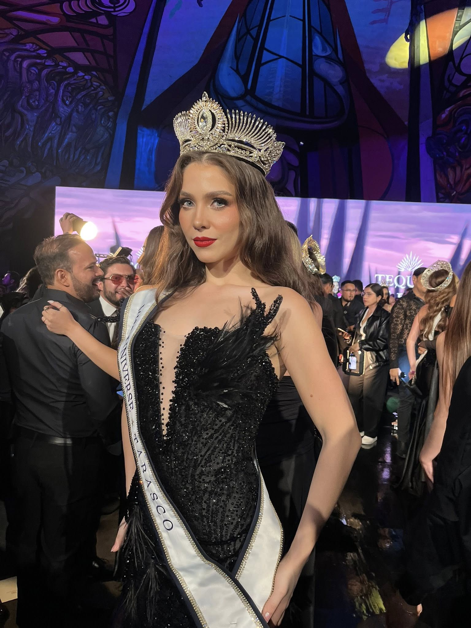 Rumbo a la corona: presentan a las 32 candidatas de miss universo méxico 2026 y revelan la sede oficial de la gran final la revista del sureste mx Fotografía En Plano Medio De Ximena Aranda, Representante De Tabasco En Miss Universo México 2026, Posando De Pie En El Polyforum Cultural Siqueiros. Luce Una Corona Plateada Con Detalles Intrincados, Cabello Largo Castaño Con Ondas Ligeras, Ojos Claros Y Labios Pintados De Rojo Intenso. Viste Un Elegante Vestido De Gala Negro Con Lentejuelas Brillantes, Un Escote Profundo Cubierto Con Malla Translúcida Y Detalles De Plumas En El Costado Izquierdo. Lleva Puesta Una Banda Blanca Cruzada Que Dice &Quot;Tabasco&Quot;. Al Fondo Se Aprecian Luces De Producción, Pantallas Con Tonos Púrpuras Y Personas Del Público O Staff En Un Ambiente De Gala Nocturna.