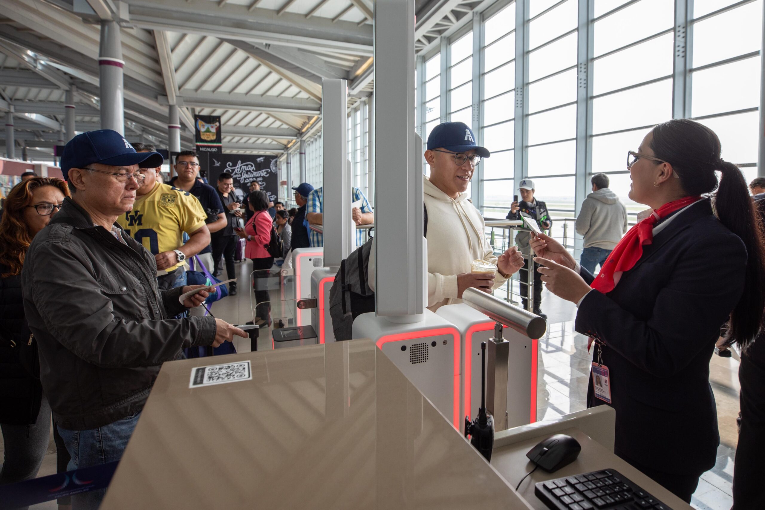 Turismo: sector alcanza récord de 5 millones 22 mil personas ocupadas en el primer trimestre de 2026 la revista del sureste mx Otografía De Reportaje En Formato Horizontal Que Muestra La Actividad Dentro De Una Moderna Terminal Aeroportuaria Iluminada Por Luz Natural Que Entra A Través De Grandes Ventanales. En El Lado Derecho, Una Agente De Aerolínea Con Uniforme Azul Marino, Pañuelo Rojo Al Cuello Y Lentes, Atiende De Manera Amable A Un Pasajero Joven Que Viste Una Sudadera Blanca Y Gorra Azul. E