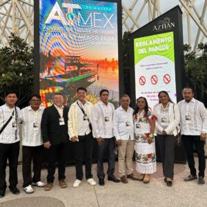 Turismo de aventura en yucatán destaca en atmex primavera 2026 la revista del sureste mx Un Grupo De Nueve Integrantes De La Delegación De Yucatán Posa Sonriente En Fila Para Una Fotografía Grupal Al Aire Libre. Visten Camisas Blancas, Guayaberas Tradicionales Y Trajes Regionales Bordados, Portando Gafetes Oficiales Del Evento. Al Fondo Se Aprecian Dos Grandes Pantallas Led, Una Con El Logotipo De Atmex Primavera Ciudad De México Y Otra Con El Reglamento Del Parque Urbano Aztlán, Flanqueadas Por Plantas Decorativas Y Una Estructura Metálica Blanca.