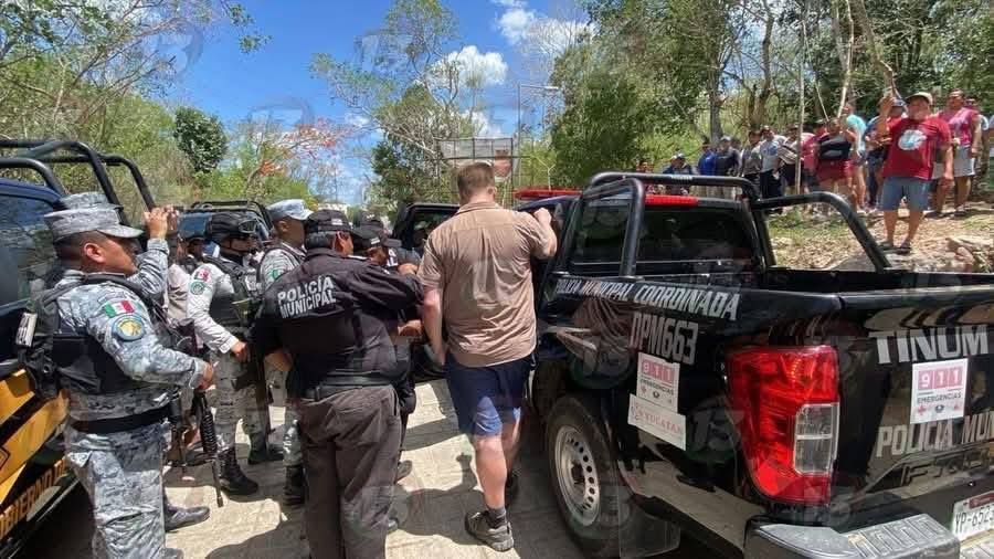 Indignación en chichén itzá: turistas extranjeros suben ilegalmente a la pirámide de kukulkán y desatan polémica la revista del sureste mx Fotografía En Plano Medio Que Muestra El Momento En Que Un Turista Extranjero De Complexión Robusta, Vestido Con Playera Tipo Polo Color Café Claro, Bermudas De Mezclilla Y Tenis, Es Escoltado Por Elementos De La Policía Municipal Coordinada De Tinum Y De La Guardia Nacional Hacia La Parte Trasera De Una Patrulla Tipo Pick-Up Negra. En La Escena Exterior, Rodeada De Árboles Y Vegetación, Se Observa A Varios Oficiales Uniformados Con Equipo Táctico Y Un Grupo De Visitantes Locales Al Fondo Observando El Procedimiento De Detención.