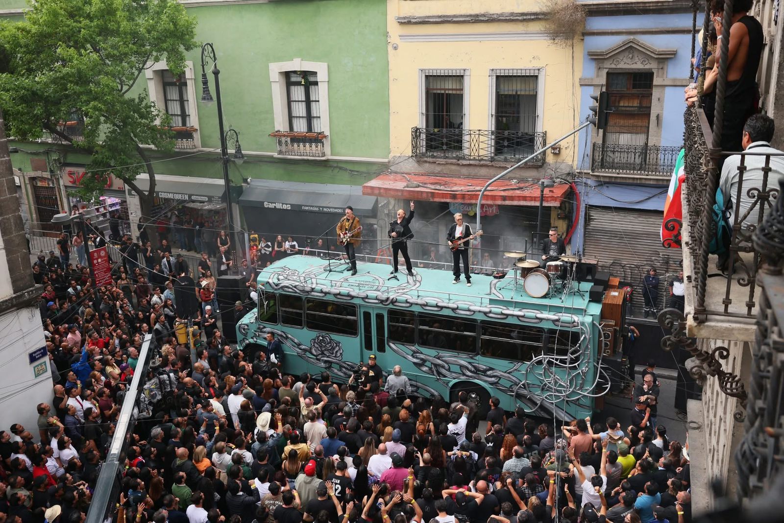 U2 en méxico: la banda irlandesa recibe invitación formal para el zócalo la revista del sureste mx Fotografía Aérea En Picado Que Captura A La Banda Irlandesa U2 Actuando Sobre El Techo De Un Autobús Escolar Color Turquesa En El Centro Histórico De La Ciudad De México. El Autobús Está Decorado Con Grafitis De Cadenas Y Una Rosa Negra, Obra Del Artista Chavis Mármol. Sobre El Vehículo Se Encuentran Bono, The Edge, Adam Clayton Y Larry Mullen Jr. Con Sus Instrumentos Y Batería. Una Multitud Masiva De Cientos De Fanáticos Rodea El Autobús En Una Calle Estrecha Flanqueada Por Edificios Históricos Con Balcones Y Fachadas De Colores Verde Y Amarillo.