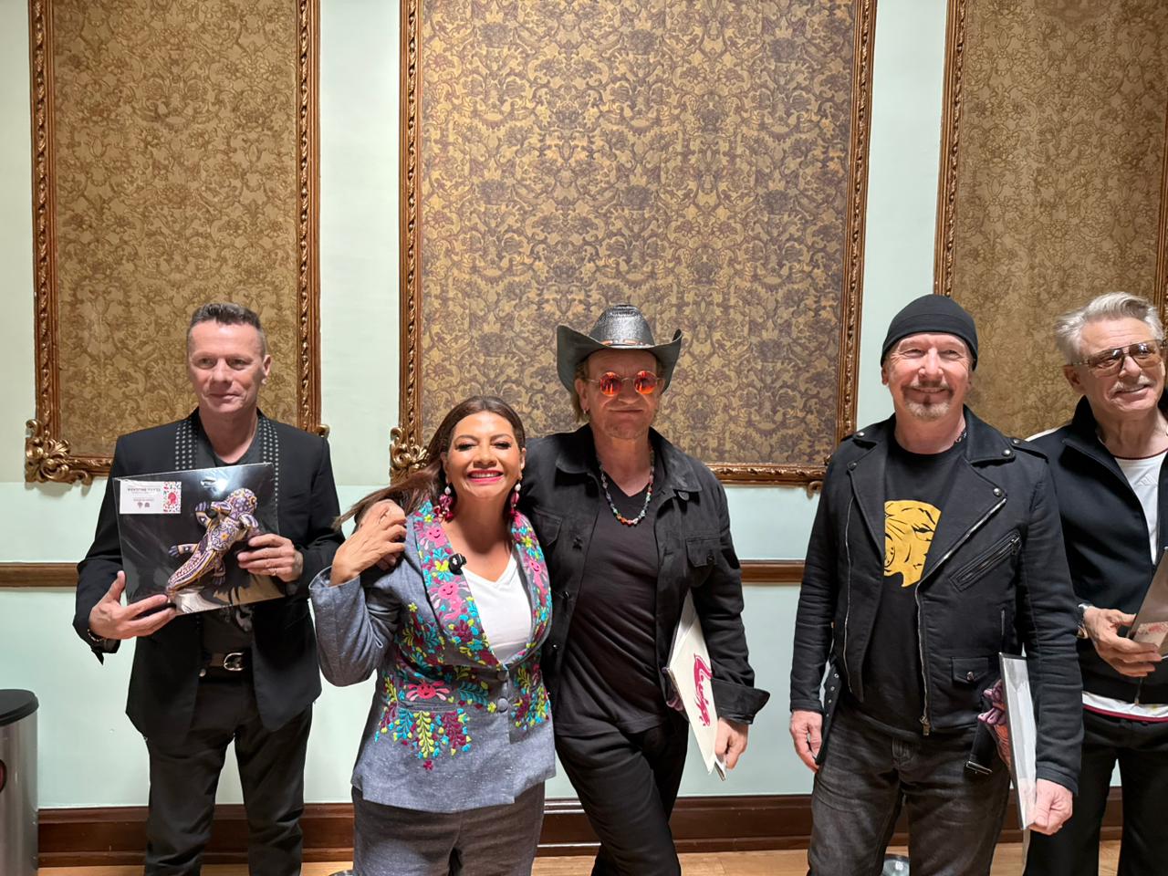 U2 en méxico: la banda irlandesa recibe invitación formal para el zócalo la revista del sureste mx Fotografía Oficial Del Encuentro Entre Los Integrantes De La Banda U2 Y Clara Brugada, Jefa De Gobierno De La Ciudad De México, En El Casino Metropolitano. En La Imagen Aparecen De Izquierda A Derecha: Larry Mullen Jr. Sosteniendo Una Figura Artesanal De Un Ajolote; Clara Brugada Sonriendo Con Un Saco Bordado Artesanal; Bono, El Vocalista, Usando Sombrero Negro Y Lentes Rojos; The Edge Con Su Clásico Gorro Negro Y Chamarra De Piel; Y Adam Clayton A La Derecha.