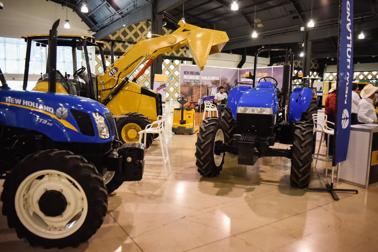 Yucatán será sede de la expo pro agro innovación 2026 la revista del sureste mx Fotografía Del Interior Del Centro De Convenciones Y Exposiciones Yucatán Siglo Xxi Durante La Expo Pro Agro Innovación 2026. En Primer Plano, Se Exhiben Tractores Agrícolas Modernos De La Marca New Holland En Colores Azul Brillante.