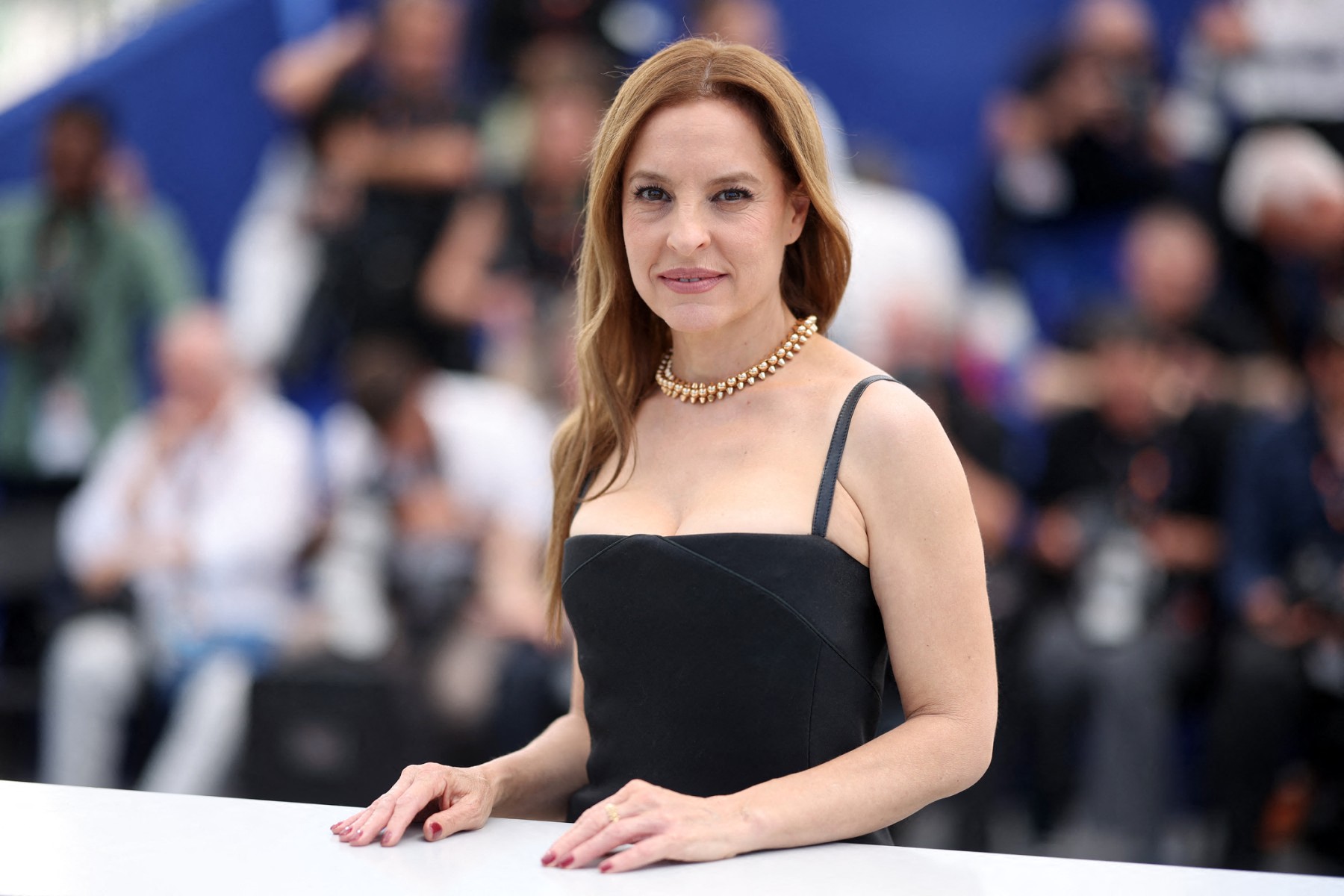 ¡histórico triunfo en cannes! Marina de tavira y el elenco de "siempre soy tu animal materno" ganan el premio a la mejor interpretación femenina la revista del sureste mx Fotografía En Plano Medio De La Actriz Mexicana Marina De Tavira Posando Sonriente Durante Una Sesión De Fotos En El Festival De Cannes. Viste Un Elegante Vestido Negro De Tirantes Delgados, Escote Recto Y Un Collar De Perlas Doradas De Varias Filas. Tiene El Cabello Castaño Claro Suelto Y Peinado De Lado. Sus Manos Descansan Sobre Una Barandilla Blanca En Primer Plano, Mientras Que El Fondo Muestra De Forma Desenfocada A Fotógrafos Y Asistentes Del Evento Sobre Un Fondo Azul Corporativo.