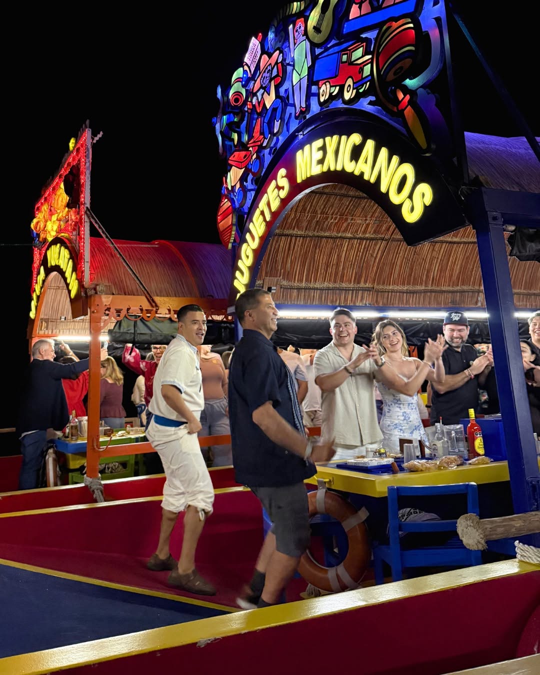 Guía de aventuras en el caribe: 4 destinos y experiencias imperdibles para sorprender a papá en cancún la revista del sureste mx Un Grupo De Personas Sonrientes Y Aplaudiendo A Bordo De Una Colorida Trajinera Tradicional Mexicana Durante Una Fiesta Nocturna En Xoximilco, Cancún. En Primer Plano, Dos Hombres Bailan Alegremente En El Centro De La Embarcación, La Cual Cuenta Con Un Arco Luminoso Decorado Que Dice &Quot;Juguetes Mexicanos&Quot;. Al Fondo Se Aprecian Otras Trajineras Iluminadas En Los Canales.