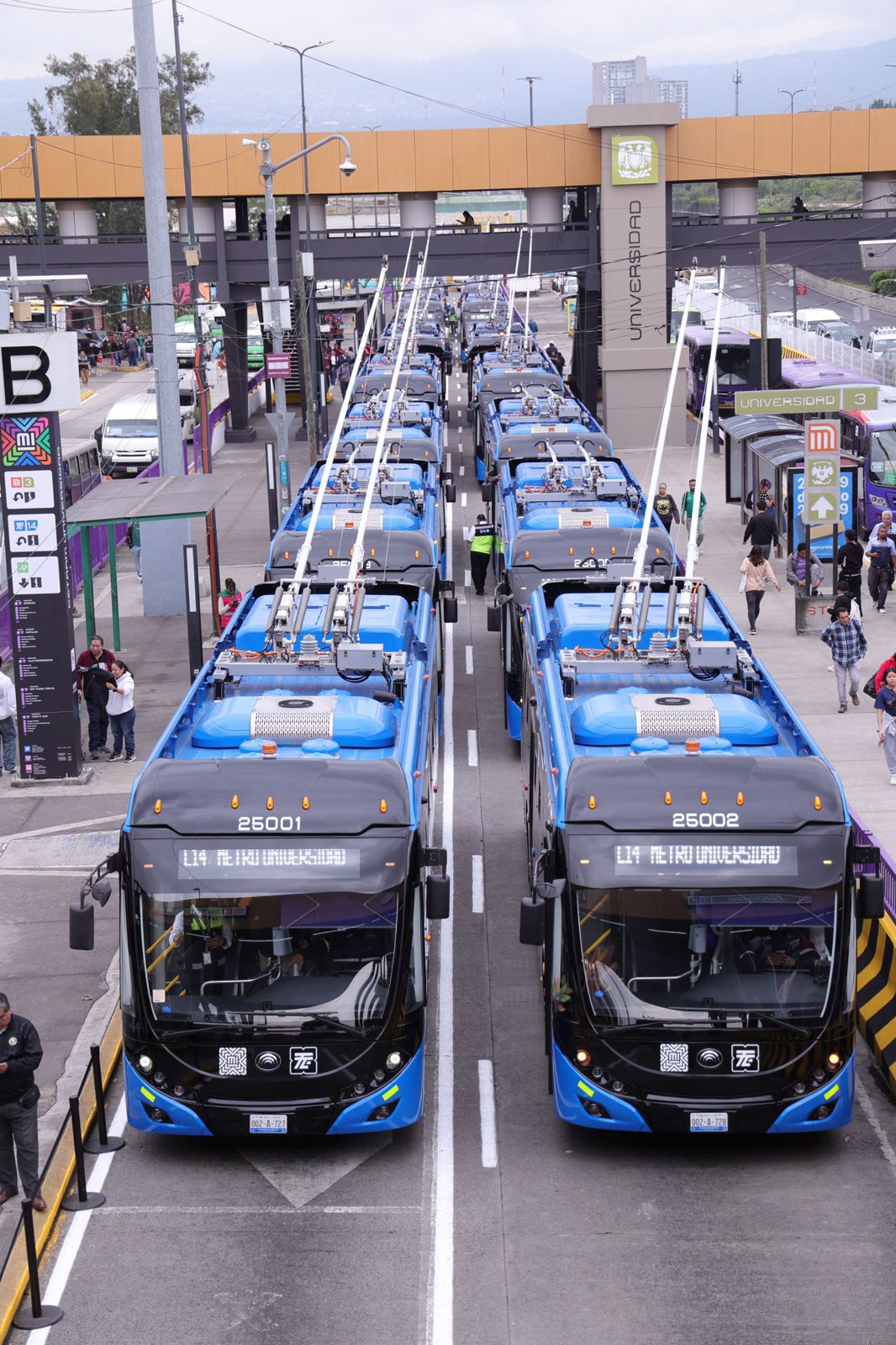 Clara brugada inaugura rutas de trolebús el chapulín y animales silvestres en cdmx la revista del sureste mx Una Toma En Perspectiva Elevada Que Muestra Dos Filas Paralelas De Modernos Trolebuses Eléctricos De Color Azul Y Negro Estacionados En La Terminal De Metro Universidad. Las Unidades Del Frente Muestran En Sus Letreros Digitales La Ruta &Quot;L14 Metro Universidad&Quot;. Los Trolebuses Están Conectados A Los Cables De La Catenaria Aérea Mediante Sus Postes De Postes De Contacto (Troles). Al Fondo Se Observa El Puente Peatonal De La Estación Universidad Y Varios Peatones Caminando Por Los Andenes Laterales.