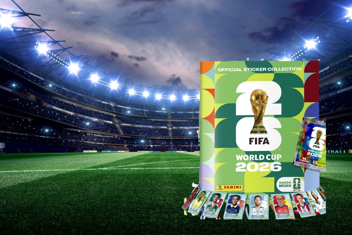 Composición Digital Que Muestra Los Productos Oficiales De Panini Sobre El Terreno De Juego De Un Gran Estadio De Fútbol Iluminado Bajo Un Cielo Nocturno Nublado. En La Mitad Derecha De La Imagen, Destaca En Primer Plano La Portada Del Álbum Oficial &Quot;Fifa World Cup 2026&Quot;, Con Un Diseño Geométrico De Colores Verde, Amarillo, Rojo Y Azul, El Trofeo Dorado De La Copa Del Mundo En El Centro Y El Logotipo De Panini Abajo A La Izquierda. Junto Al Álbum Se Observa Un Sobre De Estampas Metalizado Y Brillante. En La Base Del Álbum, Acomodados En Semicírculo, Se Muestran Varios Cromos Individuales Con Los Rostros De Futbolistas Internacionales Destacados. La Mitad Izquierda De La Imagen Muestra El Pasto Verde Del Campo De Juego, Las Tribunas Llenas De Espectadores Difuminados Y Los Potentes Reflectores Del Estadio Encendidos.