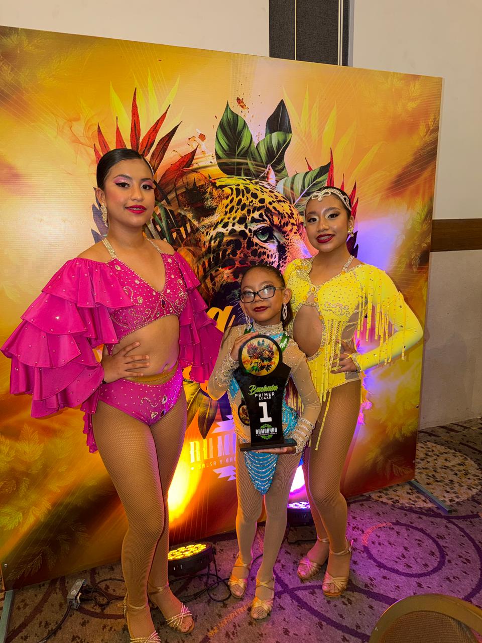Veracruz: el salsa fest 2026 suma una agenda de actividades culturales y recreativas desde temprana hora la revista del sureste mx Fotografía En Plano Medio Vertical Que Muestra A Tres Niñas Bailarinas Posando Sonrientes En Un Salón Cerrado. Visten Trajes De Baile Profesionales Con Pedrería Y Calzado De Baile Color Bronce; La De La Izquierda Usa Un Conjunto Fucsia Con Mangas De Volantes, La Del Centro (Con Lentes) Un Leotardo Azul Claro Mientras Sostiene Un Trofeo Negro Que Indica &Quot;Primer Lugar&Quot;, Y La De La Derecha Un Diseño Amarillo Con Flecos.