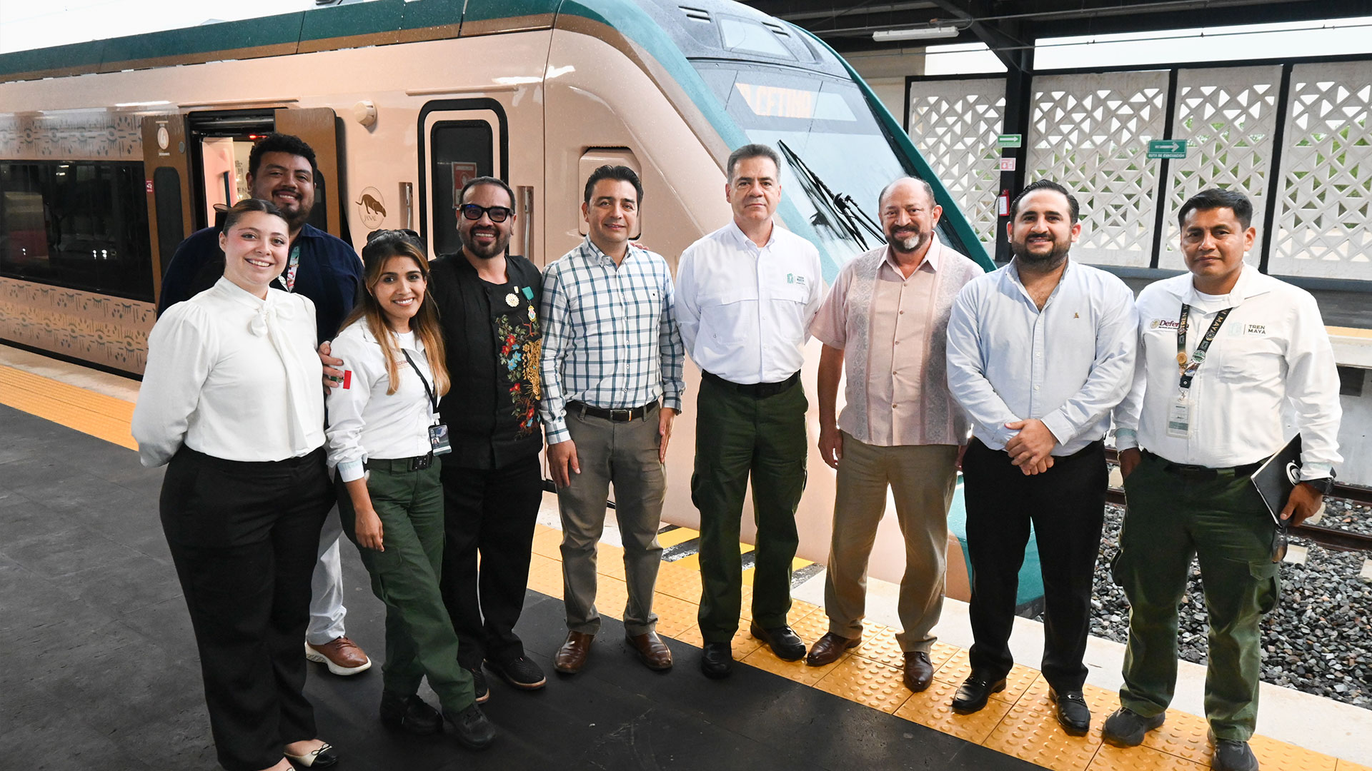 Sabores sobre rieles: el tren maya consolida la experiencia de su tren restaurante "janal" la revista del sureste mx Fotografía Grupal En Plano Entero Tomada Al Aire Libre Sobre El Andén De Una Estación Ferroviaria. Un Grupo De Nueve Personas, Integrado Por Siete Hombres Y Dos Mujeres, Posa Sonriente Frente A La Cabina Principal De Un Vagón Del Tren Maya De Color Blanco Con Franjas Verde Agua Y Detalles Dorados.