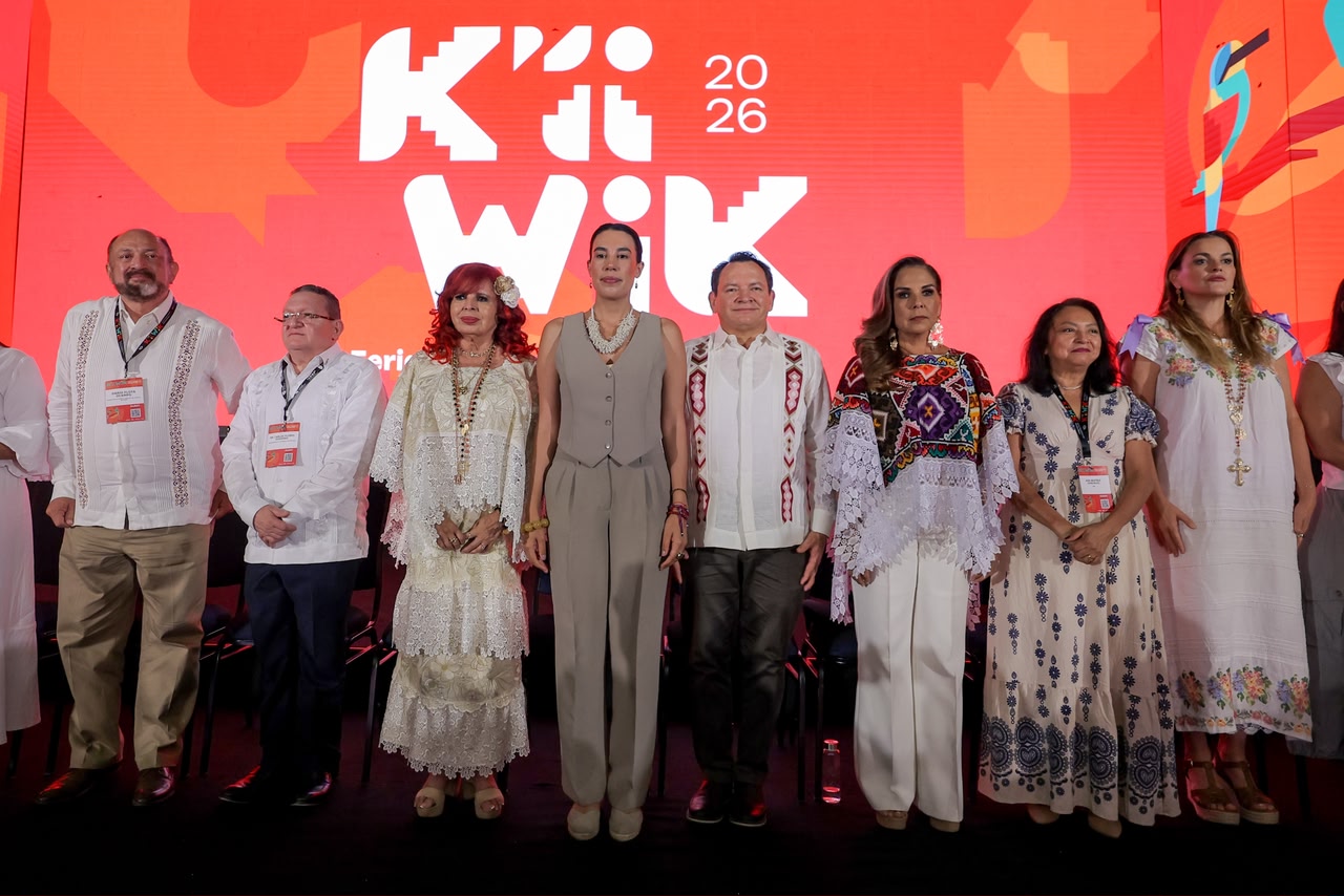 Un Presídium De Ocho Autoridades Y Funcionarias Públicas Posa De Pie En Línea Recta Sobre Un Escenario Oscuro Durante La Inauguración De La Feria Turística. Al Fondo, Destaca Una Enorme Pantalla Led De Color Rojo Brillante Con El Logotipo Oficial Del Evento En Letras Estilizadas Blancas Que Dice &Quot;K'Íiwik 2026&Quot;. De Izquierda A Derecha, Se Observa A Darío Flota Ocampo Con Guayabera Blanca