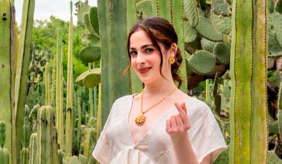 Fátima bosch en oaxaca: todo el recorrido de la miss universo rumbo a la guelaguetza 2026 la revista del sureste mx Retrato De Medio Cuerpo De La Miss Universo Mexicana Fátima Bosch En Oaxaca, Posando Sonriente En El Parque Etnobotánico Rodeada De Grandes Cactus Y Nopales Verdes. Viste Una Prenda Estilizada De Color Blanco Oaxaqueño Con Un Escote En V Pronunciado, Y Luce Joyería Artesanal Dorada Que Incluye Un Collar Con Un Dije Redondo Texturizado Y Aretes A Juego. Con Su Mano Izquierda Hace El Gesto De Un &Amp;Quot;Corazón Coreano&Amp;Quot; Con Los Dedos Hacia La Cámara. Su Cabello Está Peinado En Un Recogido Suave Con Mechones Sueltos Que Enmarcan Su Rostro. La Iluminación De Fondo Es Natural Y Suave.