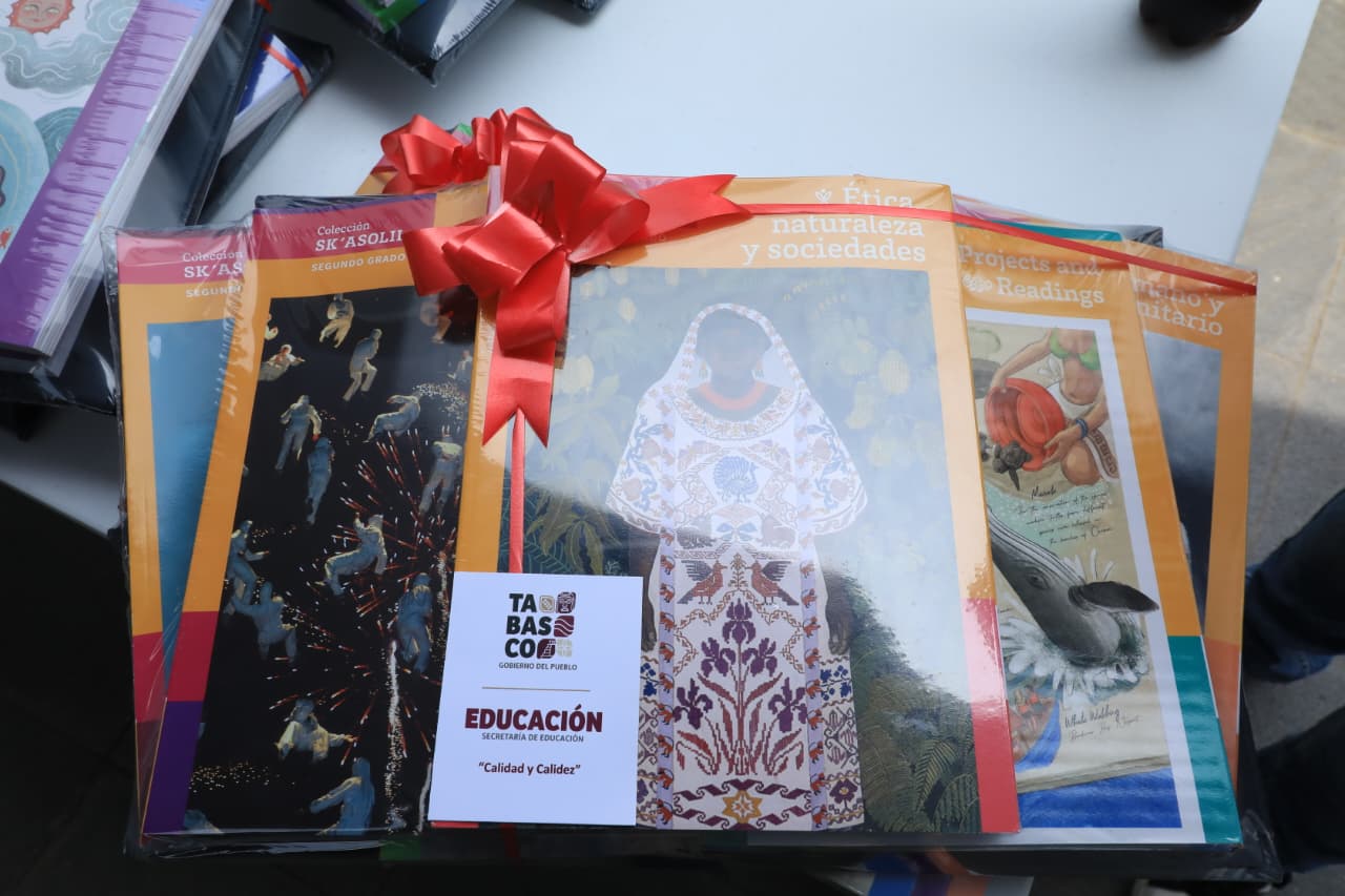 Fotografía De Primer Plano En Picada Que Muestra Un Paquete De Libros De Texto Gratuitos De La Secretaría De Educación Pública Agrupados Sobre Una Mesa. Los Libros Están Sellados En Plástico Transparente Y Decorados Con Un Gran Moño De Listón Rojo Satinado.