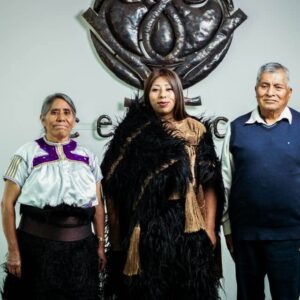 Joven indígena de chiapas rompe barreras al lograr su doctorado la revista del sureste mx Fotografía De Susi Bentzulul En El Centro, Vistiendo Indumentaria Tradicional De San Juan Chamula Con Un Chuj Negro De Lana Y Detalles Dorados, Flanqueada Por Sus Padres. Al Fondo, Se Aprecia El Logotipo Metálico Del Cesmeca.