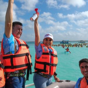 Mara lezama encabeza maratón de aguas abiertas en bacalar la revista del sureste mx La Gobernadora De Quintana Roo, Mara Lezama Espinosa, Sonríe En El Centro Mientras Levanta Una Bocina De Aire Roja Para Dar El Banderazo De Salida. Viste Jeans, Una Gorra Blanca Con El Logotipo Del Estado Y Un Chaleco Salvavidas Naranja Brillante Tipo Iii Sobre Una Camiseta Azul Con Estampados Tropicales.