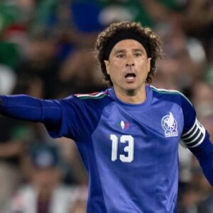 Fotografía De Cuerpo Completo Del Portero Mexicano Guillermo 'Memo' Ochoa En Pleno Partido De Fútbol. Viste El Uniforme De Guardameta Color Azul Marino De La Selección Mexicana Con El Número 13 En El Pecho Y En El Short, Medias Azules Y Tacos Color Rosa Fosforescente. Lleva Una Banda Negra En La Cabeza Y Guantes De Portero Blancos Con Detalles Rojos Y Negros.