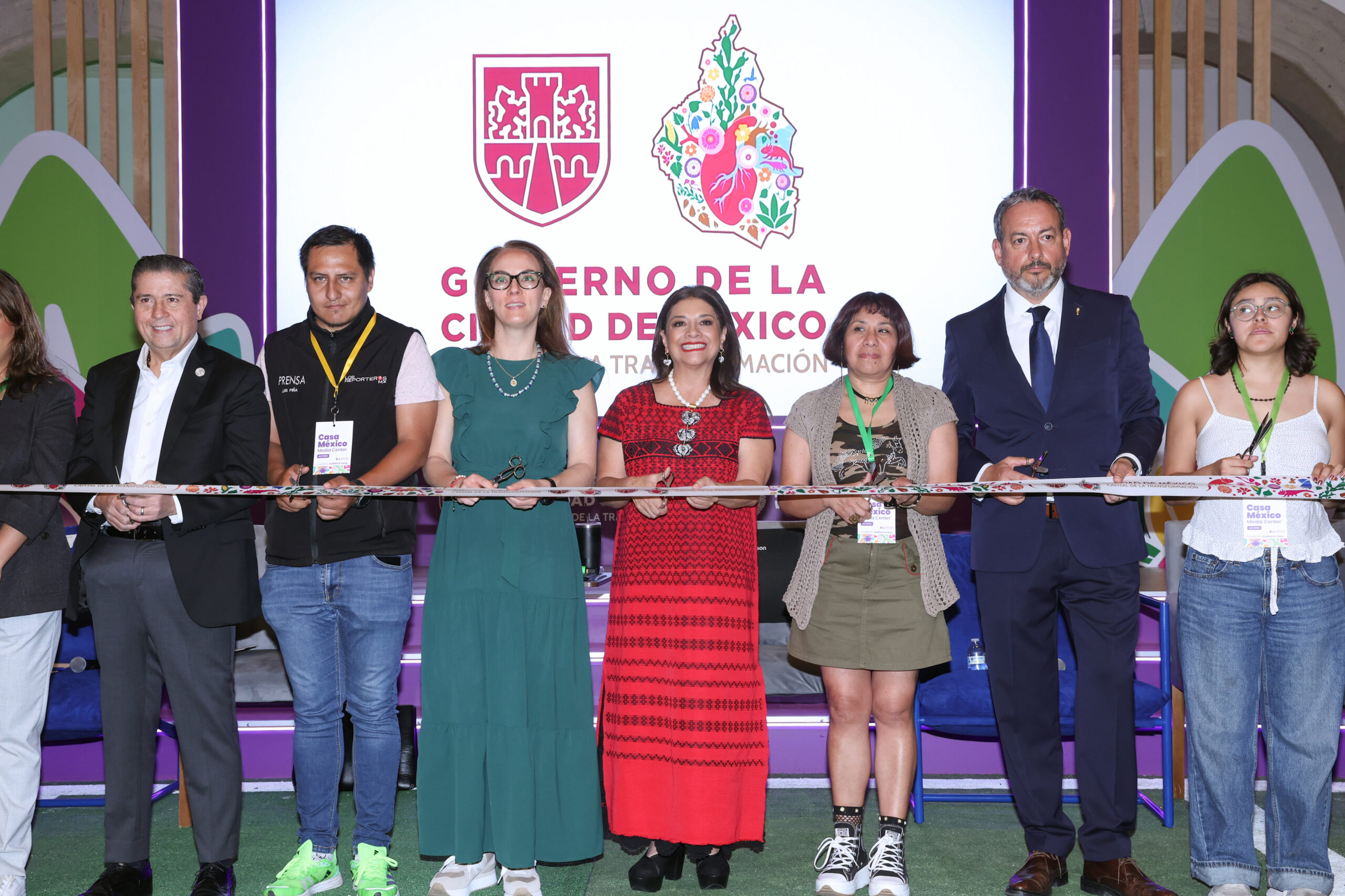 Fotografía Oficial Del Corte De Listón Inaugural De La Casa Ciudad De México: International Media Center Para El Mundial 2026. Al Centro, La Jefa De Gobierno Clara Brugada Molina Viste Un Vestido Rojo Con Bordados Tradicionales Y Sostiene Unas Tijeras. Está Acompañada A Los Lados Por Funcionarios Y Colaboradores Sosteniendo El Listón Decorado Frente A Una Pantalla Iluminada Con Los Logotipos Oficiales Del Gobierno De La Ciudad De México.