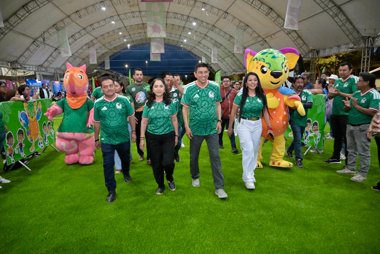 Oaxaca se pone la camiseta: inauguran el mundial social 2026 en el parque primavera la revista del sureste mx Siete Personas, Tres Mujeres Y Cuatro Hombres, Están De Pie Alineadas En Un Escenario Durante Un Evento. Seis De Ellas Visten Camisetas Verdes Idénticas Con Detalles Estampados, Excepto Una Mujer Que Lleva Una Camisa Polo Verde. Detrás De Ellas Hay Una Gran Pantalla Led Que Muestra Rostros De Personas En El Público. Un Podio De Acrílico Transparente Está A La Izquierda Con Un Micrófono Y Gráficos De Marca Que Incluyen Un Logotipo Con Un Balón De Fútbol Estilizado Y El Texto &Amp;Quot;Mundial Social 2026 Dif Oaxaca 2026&Amp;Quot; Y El Logotipo Del Dif Oaxaca.