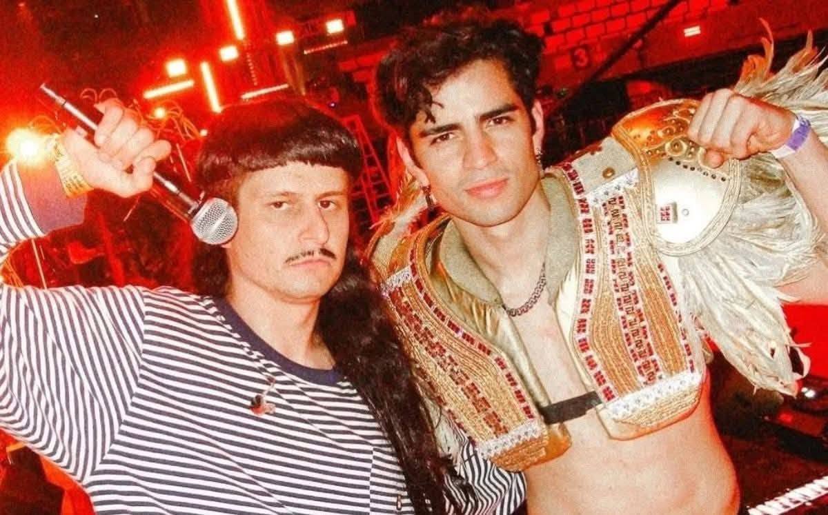Tragedia en la música: ¿quién era oliver tree, el cantante y amigo de aaron mercury que falleció en un accidente aéreo en brasil? La revista del sureste mx Otografía En Plano Medio Del Cantante Estadounidense Oliver Tree Y El Influencer Mexicano Aaron Mercury Posando Juntos En Un Evento Nocturno Iluminado Con Luces Rojas Al Fondo. A La Izquierda, Oliver Tree Viste Una Playera De Manga Larga A Rayas Blancas Y Negras, Sostiene Un Micrófono Con La Mano Derecha Y Luce Su Característico Corte De Cabello De Hongo Con Bigote. A La Derecha, Aaron Mercury Aparece Con El Torso Parcialmente Descubierto Portando Una Indumentaria Decorativa Dorada Con Bordados Rojos Y Plumas Claras Sobre El Hombro.