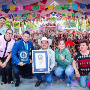 Una Fotografía Grupal En Xilitla, San Luis Potosí, Donde Autoridades Y Organizadores Sonríen En Primer Plano Sosteniendo El Certificado Oficial De Guinness World Records. Al Centro, Un Hombre Con Sombrero Vaquero Sostiene El Cuadro Del Reconocimiento Junto A Un Adjudicador Con Traje Azul Que Muestra Una Carpeta Con El Logotipo De &Amp;Quot;Guinness World Records Officially Amazing&Amp;Quot;. Al Fondo, Una Gran Multitud En Una Plaza Techada Celebra Agitando Sombreros Bajo Un Decorado De Banderines De Papel Picado Multicolor.