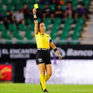 ¡orgullo nacional! Katia itzel garcía será la primera mexicana en pitar como árbitra central en un mundial varonil la revista del sureste mx La Árbitra Mexicana Katia Itzel García, Vestida Con Uniforme Oficial De Color Amarillo Y Negro, De Pie En El Terreno De Juego De Un Estadio De Fútbol. Con Determinación, Mantiene El Brazo Derecho Completamente Extendido Hacia Arriba Mostrando Una Tarjeta Amarilla. Al Fondo Se Aprecian Las Gradas Del Estadio Difuminadas Y Publicidad Perimetral En La Cancha.
