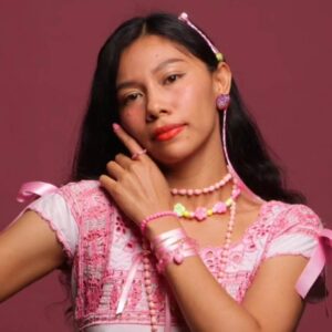 Azalea báalam: la voz mexicana que revitaliza el maya y el náhuatl a ritmo de pop la revista del sureste mx : Retrato De La Cantautora Mexicana Azalea Báalam Vistiendo Una Blusa Blanca Con Bordados Y Accesorios Rosas, Sobre Un Fondo Color Vino.