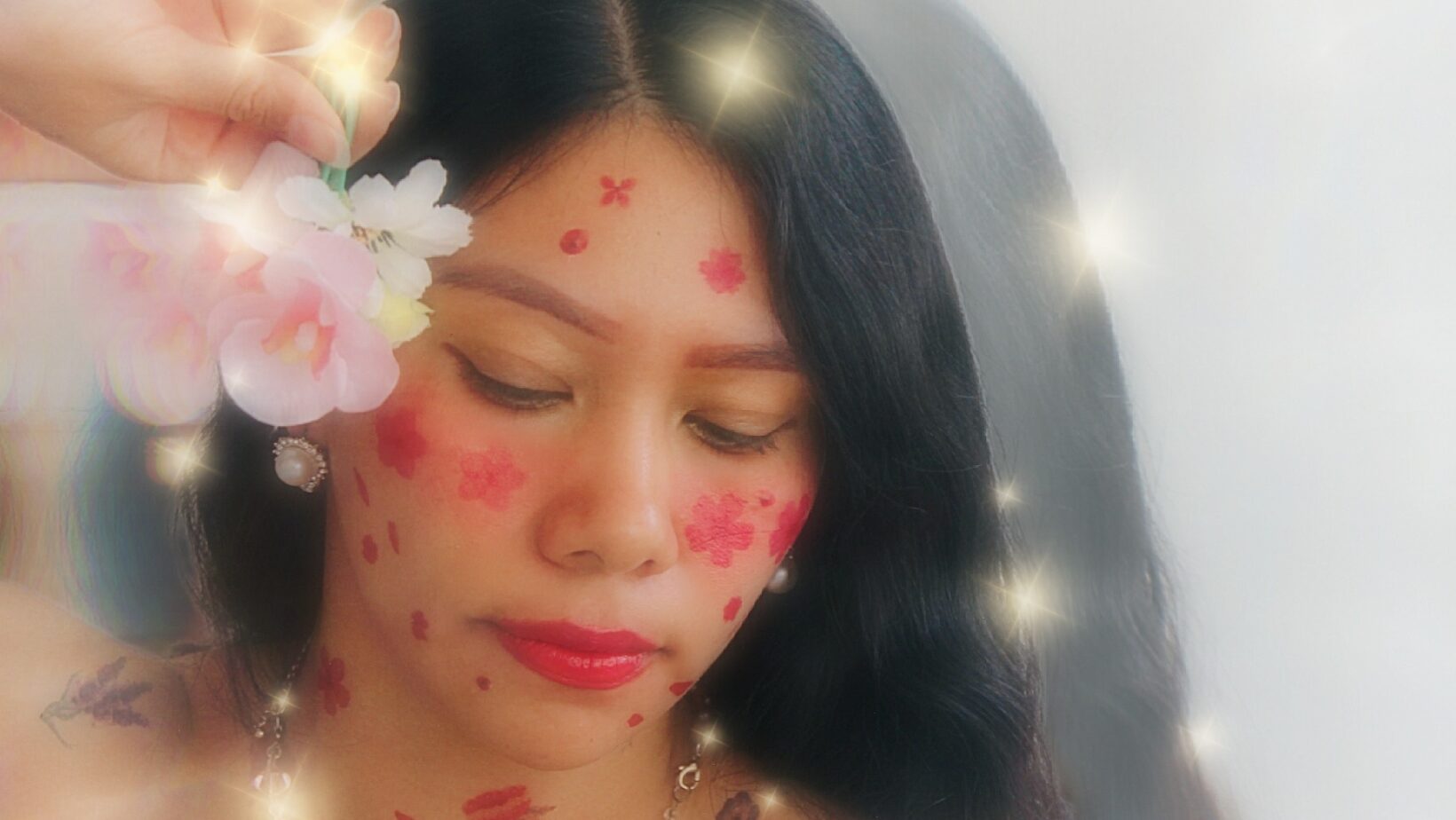 Azalea báalam: la voz mexicana que revitaliza el maya y el náhuatl a ritmo de pop la revista del sureste mx Primer Plano Artístico De Azalea Báalam Con Decoraciones Florales Pintadas En Su Rostro, Un Efecto De Destellos Brillantes Y Una Flor En La Mano.