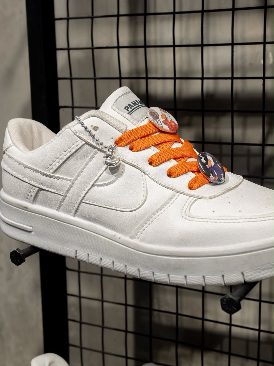 Un Tenis Blanco Panam De Edición Limitada Del Pato Merlín Con Agujetas Naranjas, Pines Ilustrados Y Un Dije Metálico De Pato.