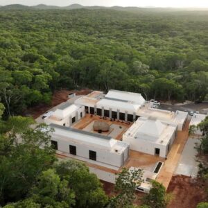Inauguran dos nuevos museos para fortalecer el legado de la cultura maya en yucatán la revista del sureste mx Vista Aérea Del Museo Arqueológico Del Puuc En Kabah. Un Moderno Complejo Blanco De Varios Edificios, Con Cubiertas Piramidales Bajas Y Un Patio Central Que Rodea Una Gran Estructura De Techo De Paja, Está Enclavado En Medio De Una Densa Selva De Copas De Árboles De Color Verde Intenso Bajo Un Cielo Brumoso. El Sol Incide De Frente En Las Fachadas, Realzando Sus Formas Geométricas. Un Camino De Grava Se Extiende Hasta El Complejo.