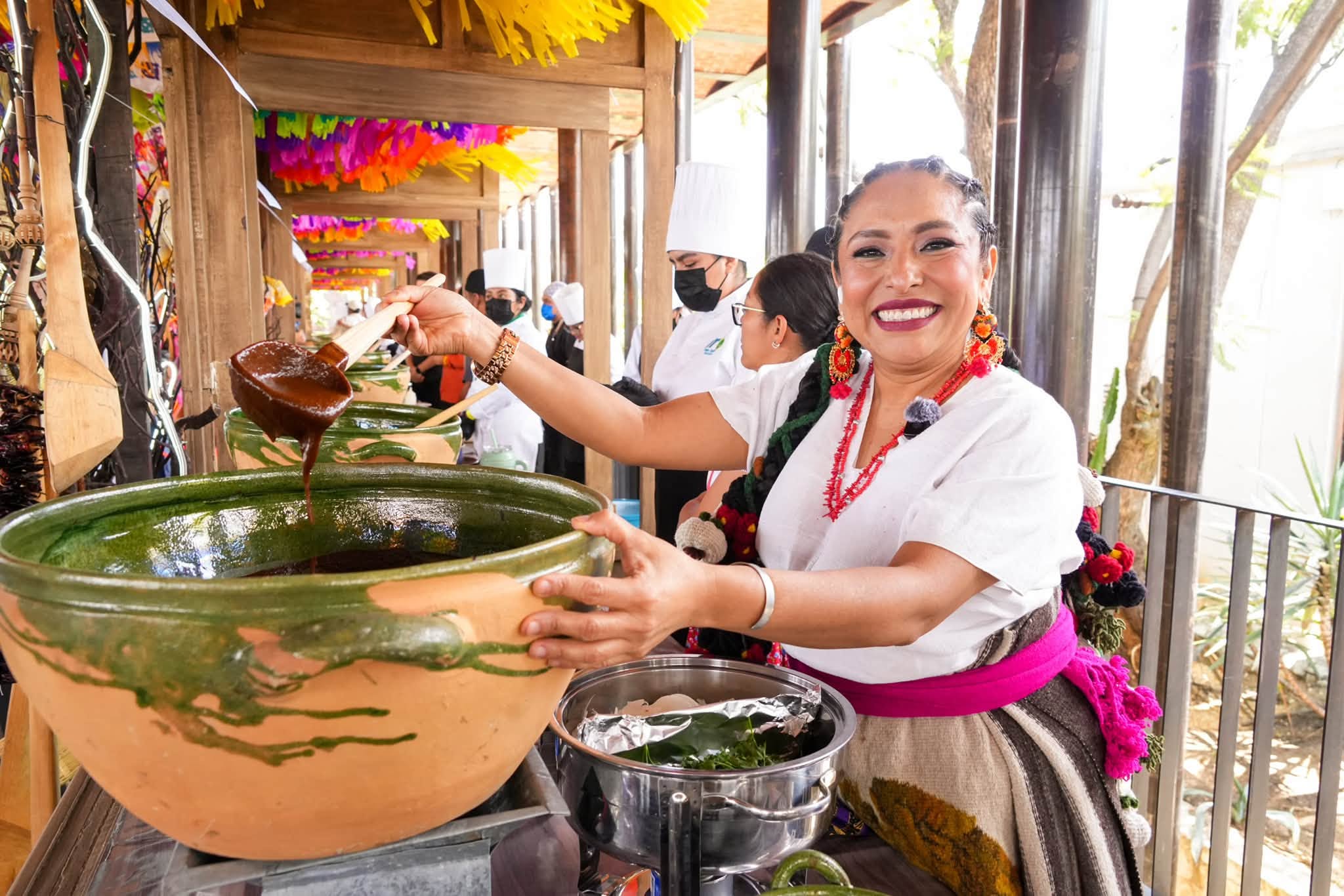 Oaxaca enaltece su riqueza gastronómica con el festival de los moles 2026 la revista del sureste mx Oaxaca Enaltece Su Riqueza Gastronómica Con El Festival De Los Moles 2026 — Cocinera Tradicional Vestida Con Traje Típico Sonríe Mientras Mezcla Una Gran Cazuela De Barro Con Mole Artesanal Utilizando Un Cucharón De Madera.