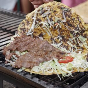 Tlayuda Oaxaqueña Tradicional Con Tasajo, Col Y Quesillo Calentándose Sobre Una Parrilla Al Carbón Durante La Feria De La Tlayuda.